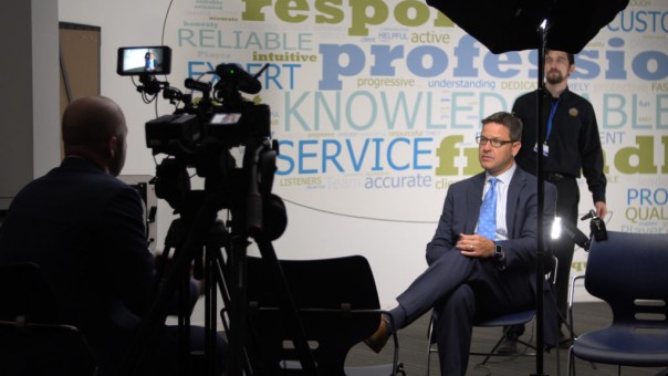 Take a behind-the-scenes glimpse of a man being interviewed, with the foreground featuring a silhouette of cameras.
